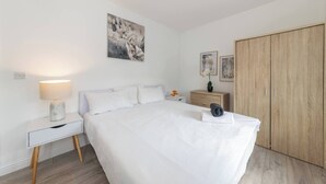 A bedroom with a large bed, a nightstand with a lamp, a wooden wardrobe, and a painting on the wall. - Ibex House Cozy Modern 2-bed Flat Free Parking (Reading)