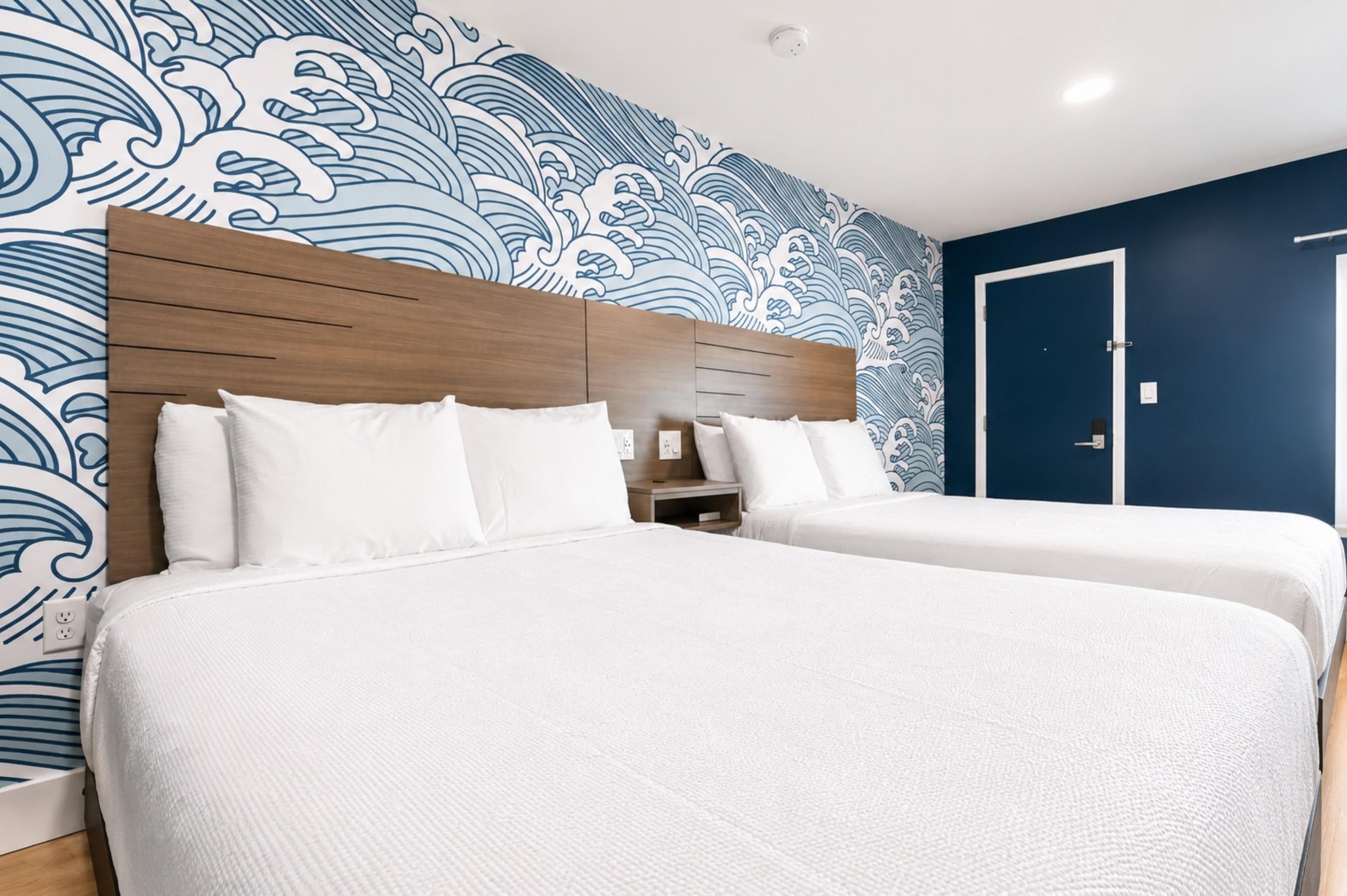 Quarto de hotel com uma cama grande, uma cama menor e uma mesa de cabeceira.