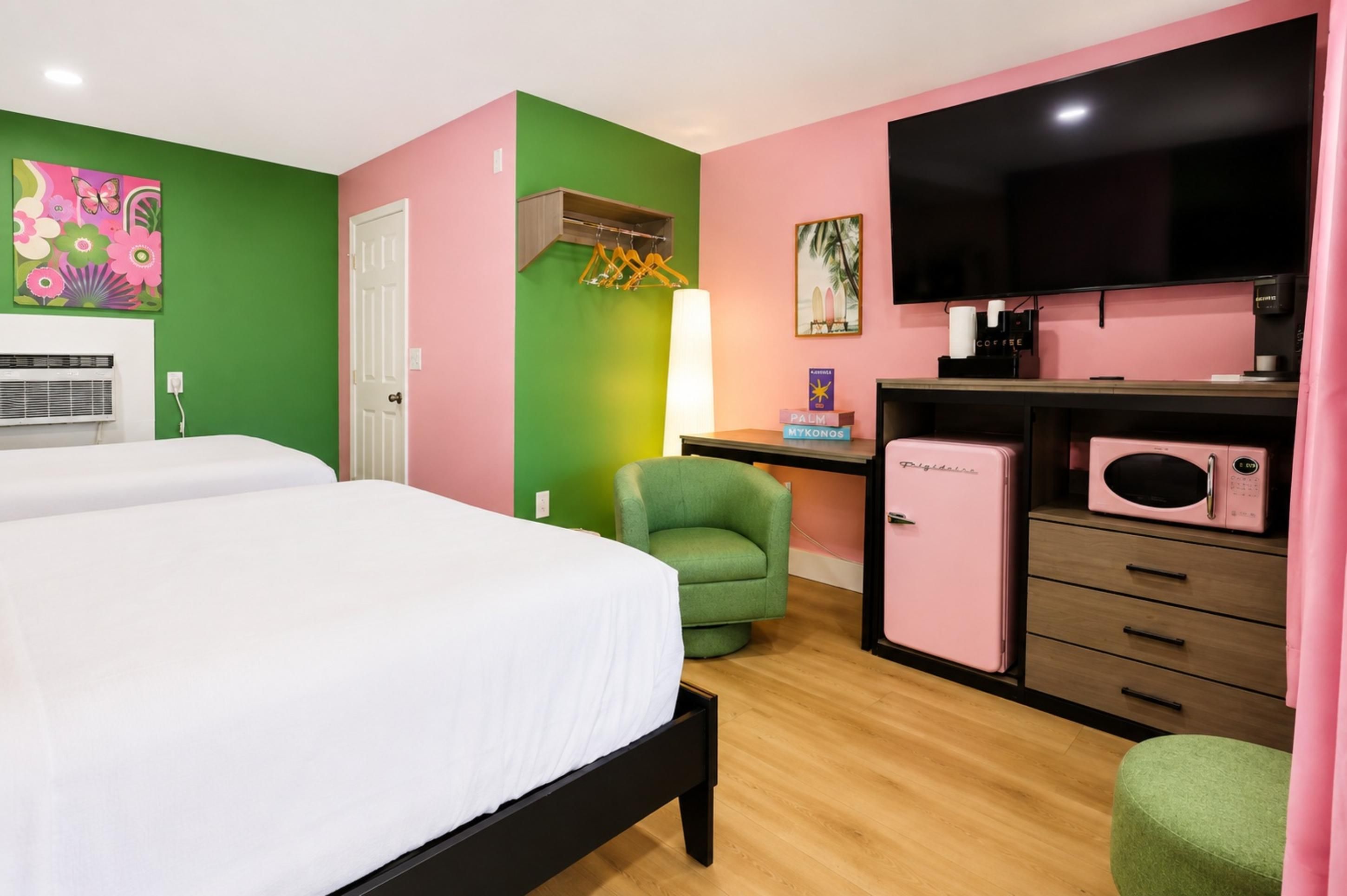 A hotel room with two beds, a desk with a computer, a TV, a small fridge, and a chair.