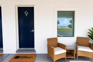 A room with a dark blue door marked with the number 9, wicker chairs with white cushions, a small table, and a view of a beach through a window. - The Blu Boutique Motel (Port St. Joe)