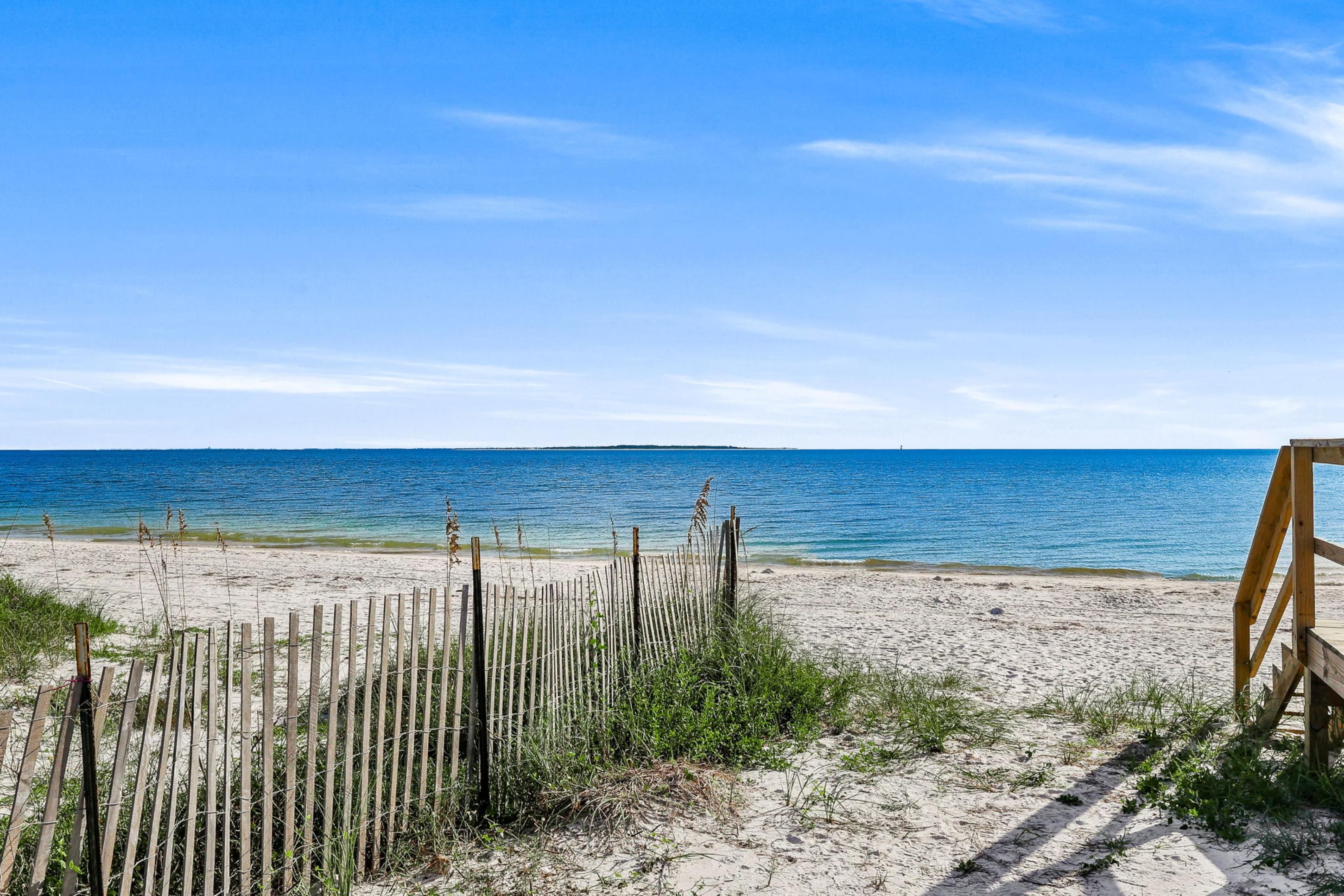 A beach with a wooden fence and a bench, leading to the ocean.