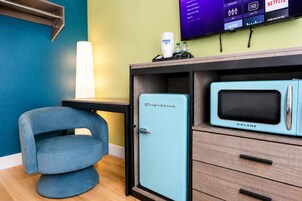 A room with a blue chair, a vintage-style microwave, and a television displaying various streaming services.