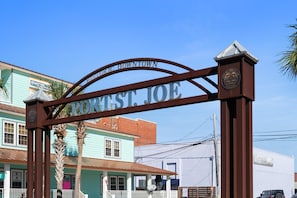Un arco de metal con la inscripción 'PORT OF PORT ST. JOE', que da paso a un edificio de fachada verde y porche blanco.