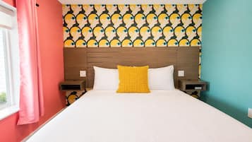 Habitación de hotel con cama, cabecero, dos mesitas de noche, ventana con cortinas y un papel tapiz estampado.