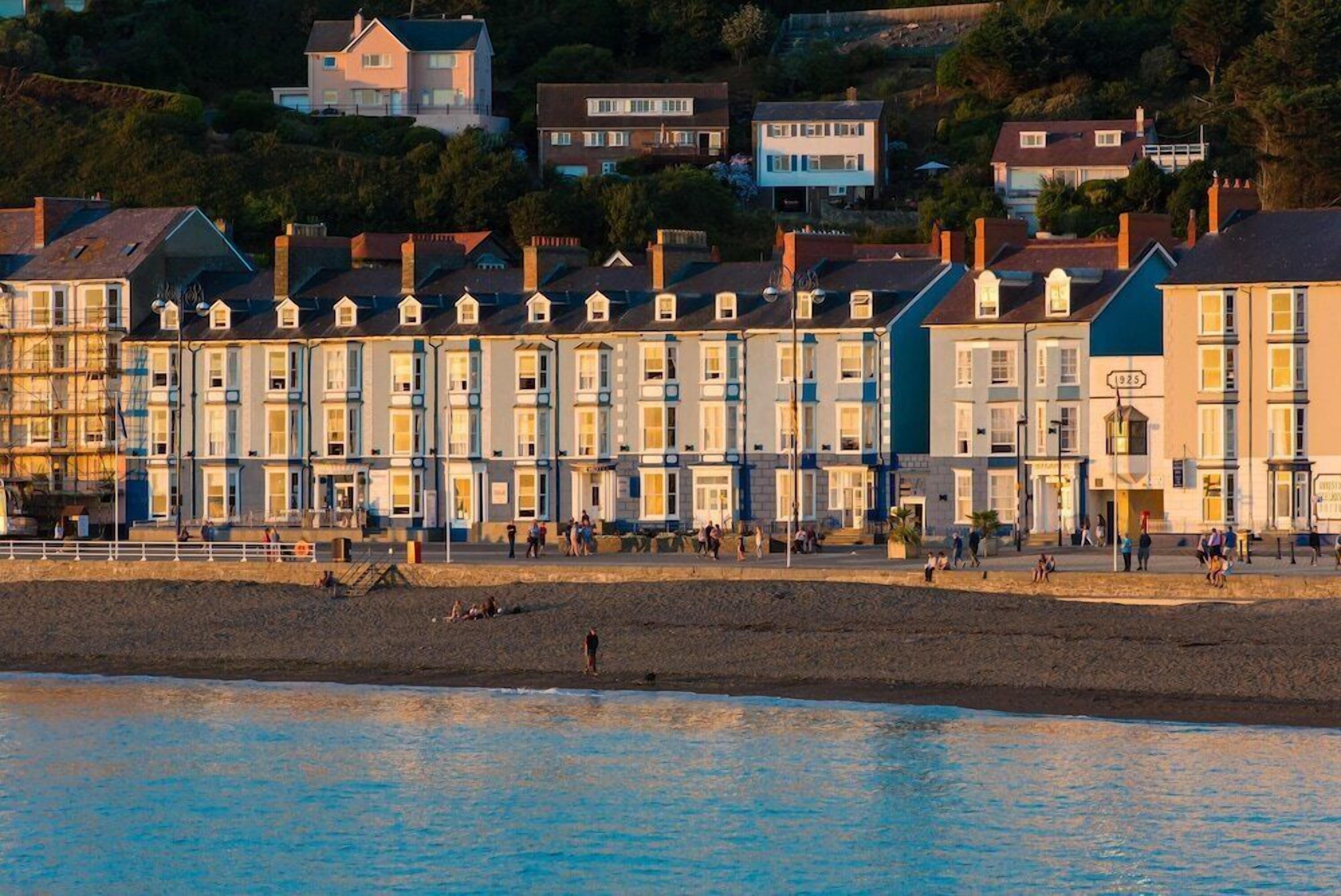 A row of terraced houses along a beach with people walking on the promenade.