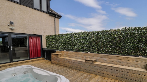 A wooden deck with a hot tub, a red door, and a hedge wall. - The Wendover (Abergele)