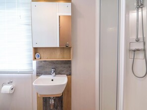 Une salle de bain avec un lavabo blanc, un miroir, une douche et des toilettes.