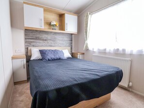 A bedroom with a bed, a nightstand, a dresser, a window with curtains, and a wall-mounted shelf with a vase. - The Retreat (Holywell)