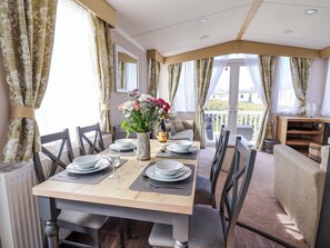 A dining area with a table set for four, chairs, a vase with flowers, and a view of the outdoors. - The Retreat (Holywell)