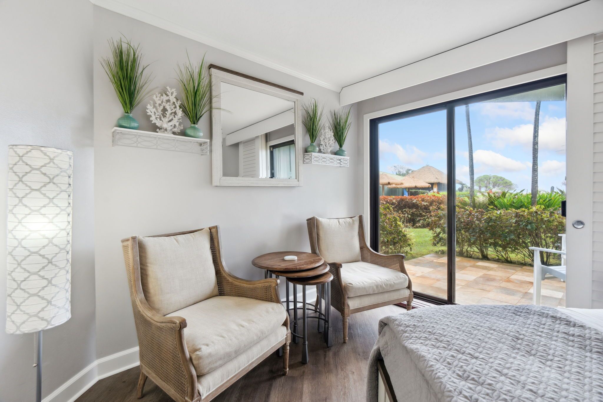 Une chambre moderne avec une grande fenêtre, des meubles en osier, une table ronde et des plantes décoratives.