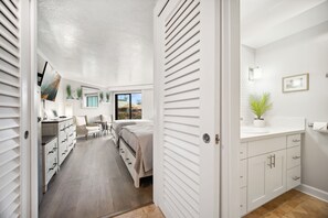 Un dormitorio con cama, mesitas de noche y un escritorio con silla. Se ve un ventanal con vistas al exterior.