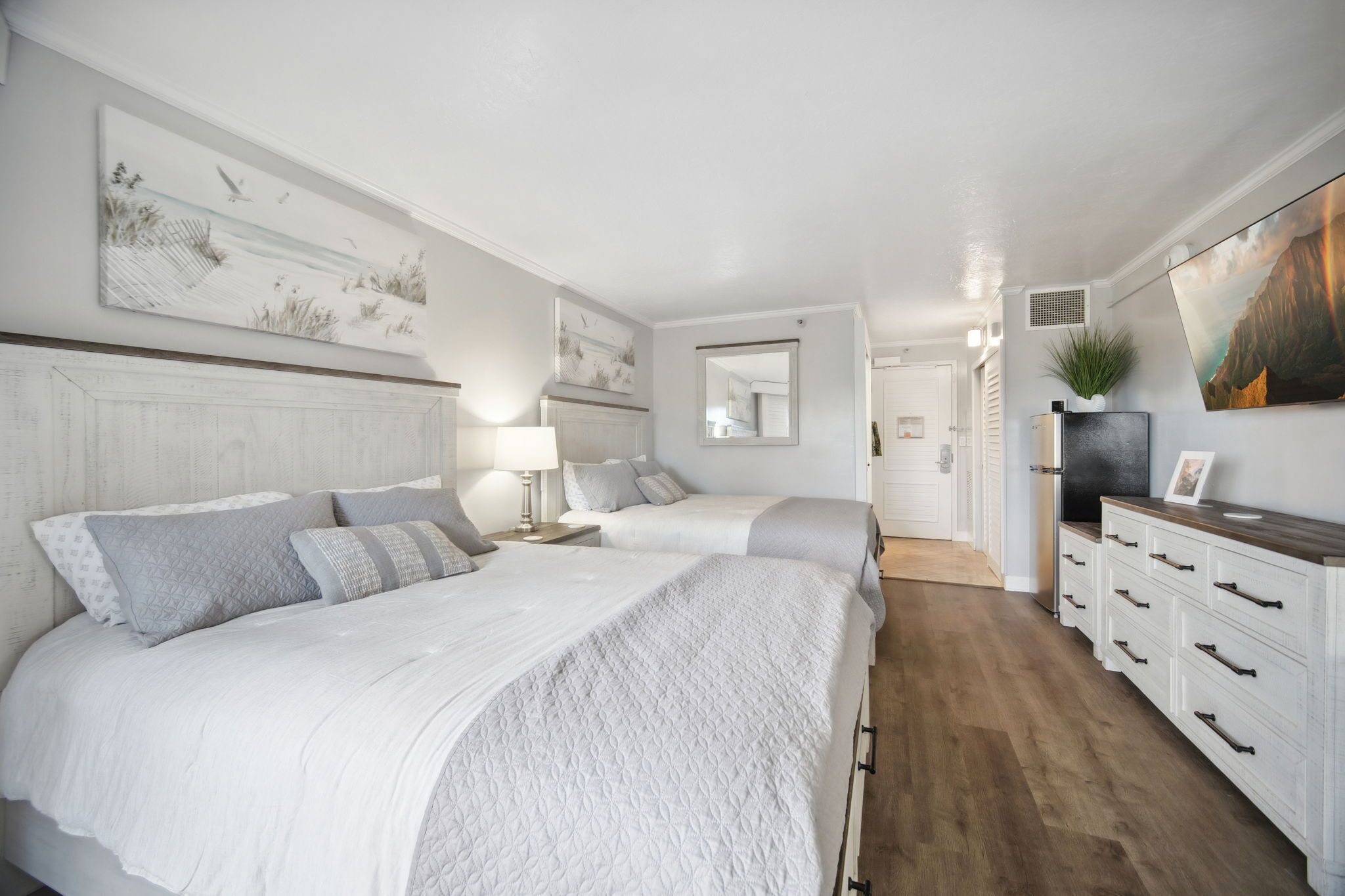 Une chambre avec deux lits, une commode, un téléviseur et des œuvres d’art accrochées aux murs.