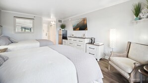 Habitación de hotel con dos camas, un tocador, una silla y un cuadro en la pared.