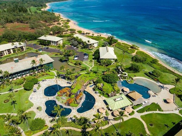 Un resort con varias piscinas, una playa y abundante vegetación.