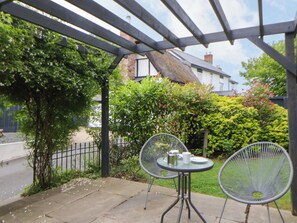 Eine Terrassengruppe im Freien mit einem Metalltisch und zwei Stühlen, umgeben von Grünpflanzen und einem Haus im Hintergrund.