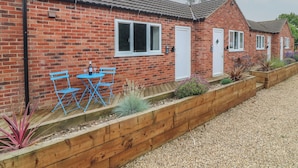 Une maison en briques avec un toit en tuiles, une porte d’entrée et un petit patio avec une table et des chaises.