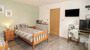 Une chambre à coucher comprenant un lit, une table de chevet, une lampe, une armoire, un téléviseur et un bureau avec un ordinateur.