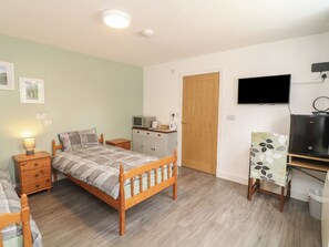 Ein Schlafzimmer mit Bett, Nachttisch, Lampe, Kleiderschrank, Fernseher und einem Schreibtisch mit Computer.