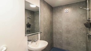 Une salle de bain avec un lavabo blanc, un miroir, une douche équipée d’un pommeau de douche à main et un sol bleu.