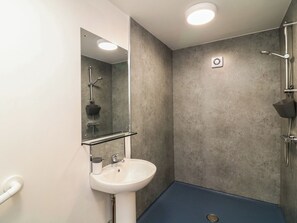 Ein Badezimmer mit einem weißen Waschbecken, einem Spiegel, einer Dusche mit Duschbrause und einem blauen Boden.