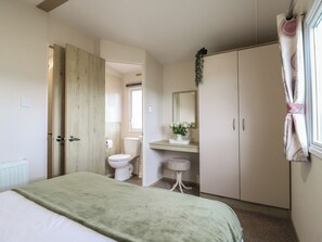 A bedroom with a bed, a wardrobe, a bathroom with a toilet, and a window with curtains. - Forest Retreat - Fo26 (Saxmundham)