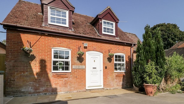 A red brick cottage with a white door, two windows, and a sign that reads 'The Cottage.' - The Cottage (Salisbury)