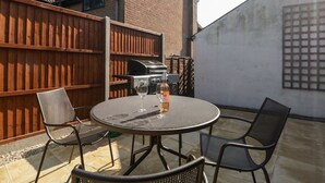 An outdoor patio with a round table and chairs, a barbecue grill, and a wooden fence. - The Cottage (Salisbury)