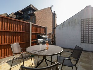 Eine Terrasse im Freien mit einem runden Tisch und Stühlen, einem Grill und einem Holzzaun.