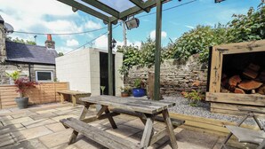 Une terrasse extérieure avec une table en bois et des bancs, entourée de murs en pierre et de plantes en pot.