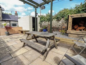 Eine Terrasse im Freien mit einem Holztisch und Bänken, umgeben von Steinmauern und Blumentöpfen.