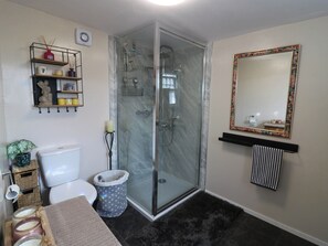 A bathroom with a glass-enclosed shower, a toilet, a sink with a mirror, and a shelf with toiletries. - The Cabin (Kirkcaldy)