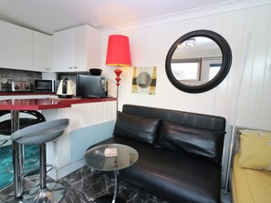 A compact living space with a kitchenette, a black leather sofa, a glass coffee table, and a red floor lamp. - The Cabin (Kirkcaldy)