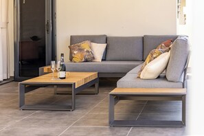 A modern living area with a grey sofa, two wooden side tables, and a glass door leading to a balcony. - Villa Mambo Royale - walking distance Mambo Beach (Willemstad)