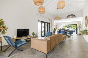 A modern living room with a flat-screen TV, comfortable seating, and a dining area with a large window. - Villa Mambo Royale - walking distance Mambo Beach (Willemstad)