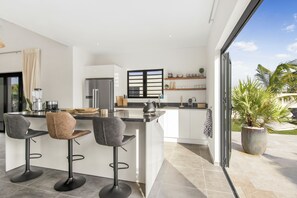 A modern kitchen with a bar area, a large window, and a potted plant. - Villa Mambo Royale - walking distance Mambo Beach (Willemstad)
