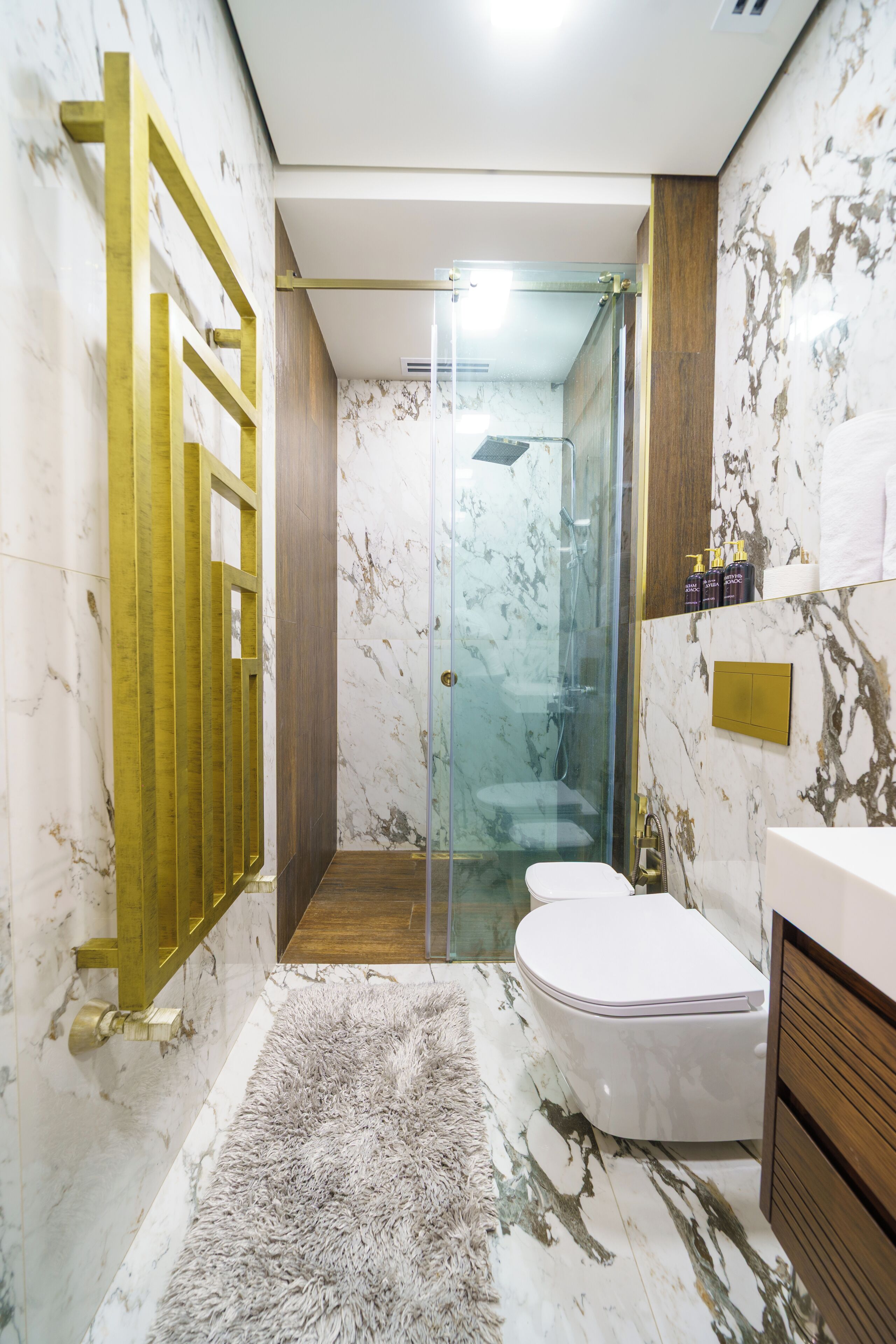 A modern bathroom with a glass shower enclosure, a wooden floor, and marble walls.