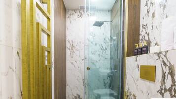A modern bathroom with a glass shower enclosure, a wooden floor, and marble walls.