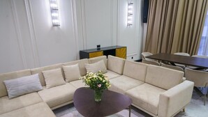 Ein modernes Wohnzimmer mit einem beigefarbenen Ecksofa, einem dunklen Couchtisch und einem Essbereich mit Tisch und Stühlen.