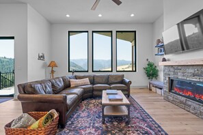 A modern living room with a leather sectional sofa, a fireplace, and a large window overlooking a mountainous landscape. - Brand-New Mountain Retreat Sleeps 8 (Palisades)