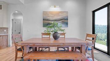 A dining area with a wooden table, chairs, a vase with greenery, and a painting on the wall.