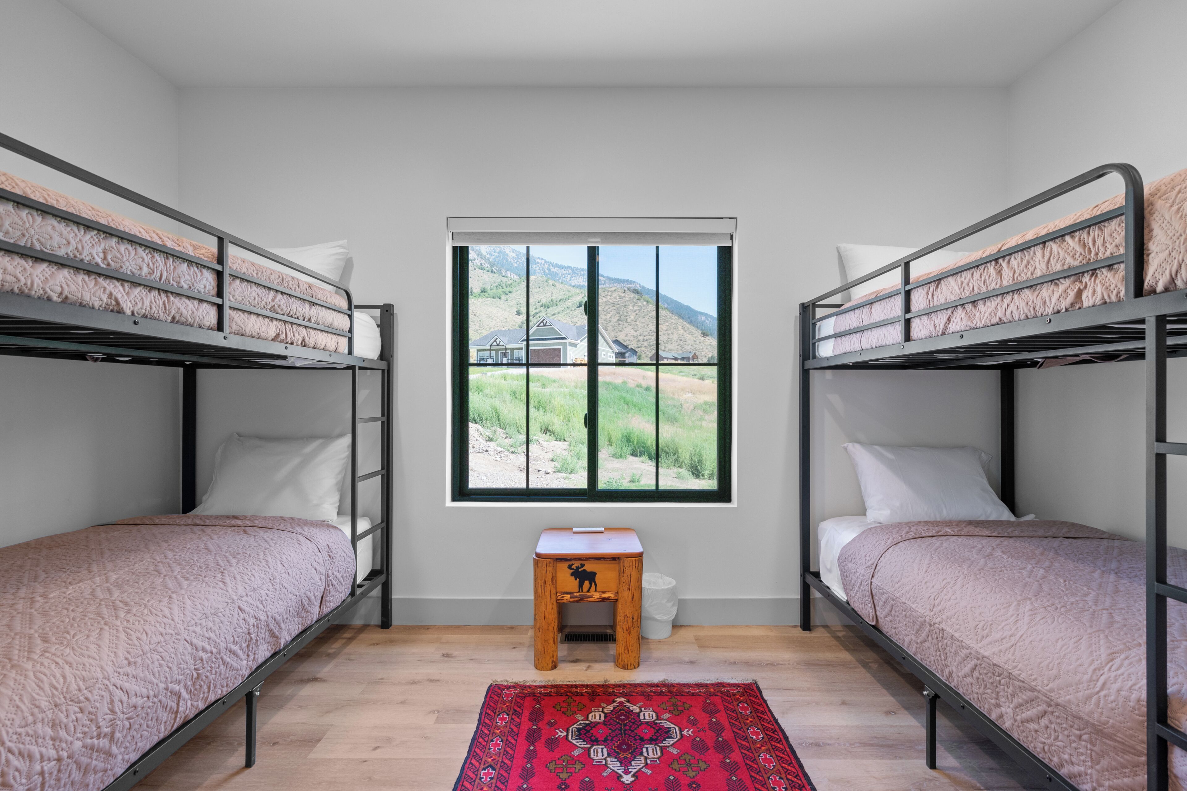 A room with bunk beds, a small stool, and a window with a view of a mountain landscape.