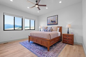 A bedroom with a wooden bed, two bedside tables, a nightstand, a ceiling fan, and a large window with a view of the mountains. - Brand-New Mountain Retreat Sleeps 8 (Palisades)