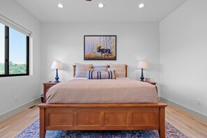 A bedroom with a wooden bed, two bedside tables, a large window, and a wall-mounted painting. - Brand-New Mountain Retreat Sleeps 8 (Palisades)
