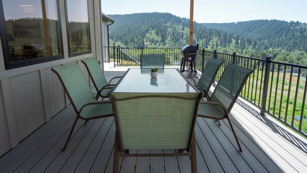 Ein überdachter Außenbereich mit Tisch und Stühlen, mit Blick auf ein bewaldetes Tal.