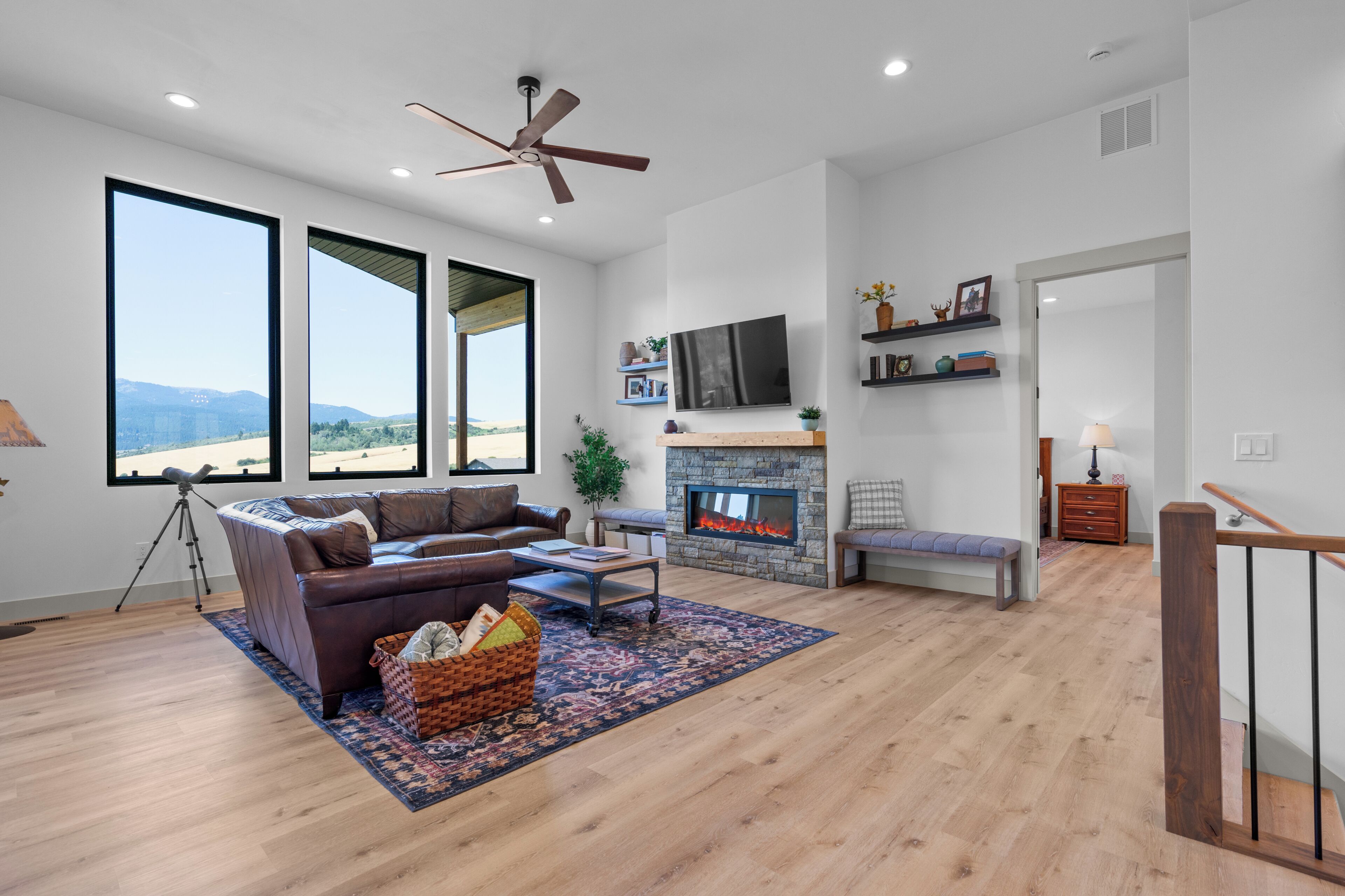 A spacious living room with a large window, a fireplace, and a ceiling fan.