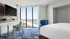 Ein Hotelzimmer mit Bett, Schreibtisch, Stuhl, Fernseher und einem großen Fenster mit Blick auf den Strand.