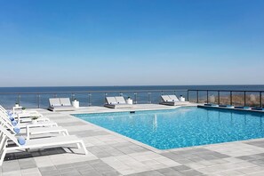 Ein Pool auf dem Dach mit weißen Liegestühlen und freiem Blick auf den Ozean.