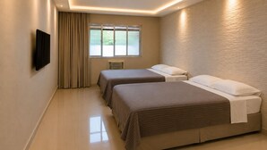 Quarto de hotel com duas camas, uma televisão na parede e uma janela com cortinas.
