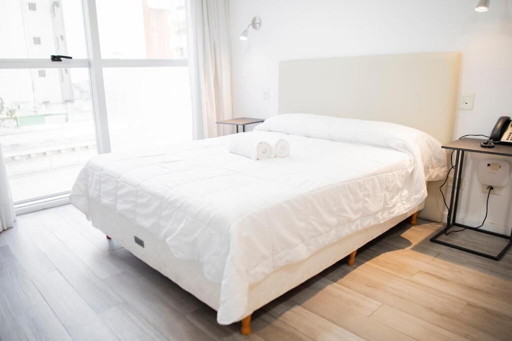 Una habitación de hotel con una cama grande, una mesita de noche con lámpara y vistas por la ventana.