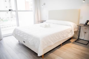 Una habitación de hotel con una cama grande, una mesita de noche con lámpara y vistas por la ventana.